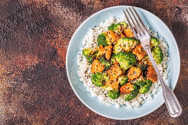 A close-up of a budget-friendly and high-protein meal: a plate with well-cooked chicken thighs, a generous portion of brown rice, and a vibrant side of steamed broccoli.